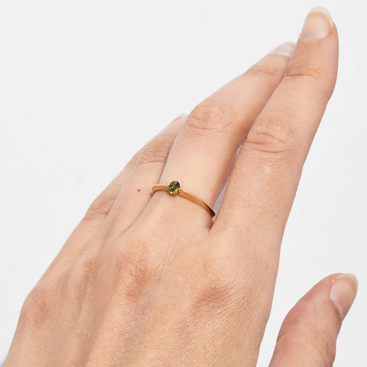 A ring on a finger viewed from the top, showcasing the prong-set oval Australian sapphire on the gold band.