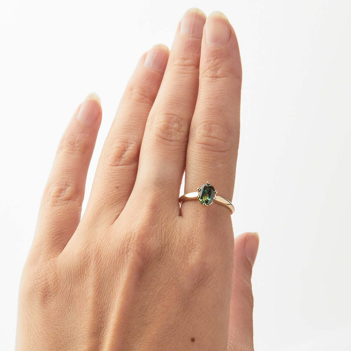 A hand modeling a yellow gold ring with an oval Australian sapphire and a knife-edge band detail.