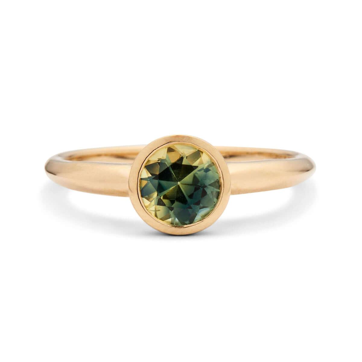 Frontal perspective of the 'Lou' ring with a bicolor sapphire in a bezel setting, set on a knife-edge gold band, against a white backdrop.