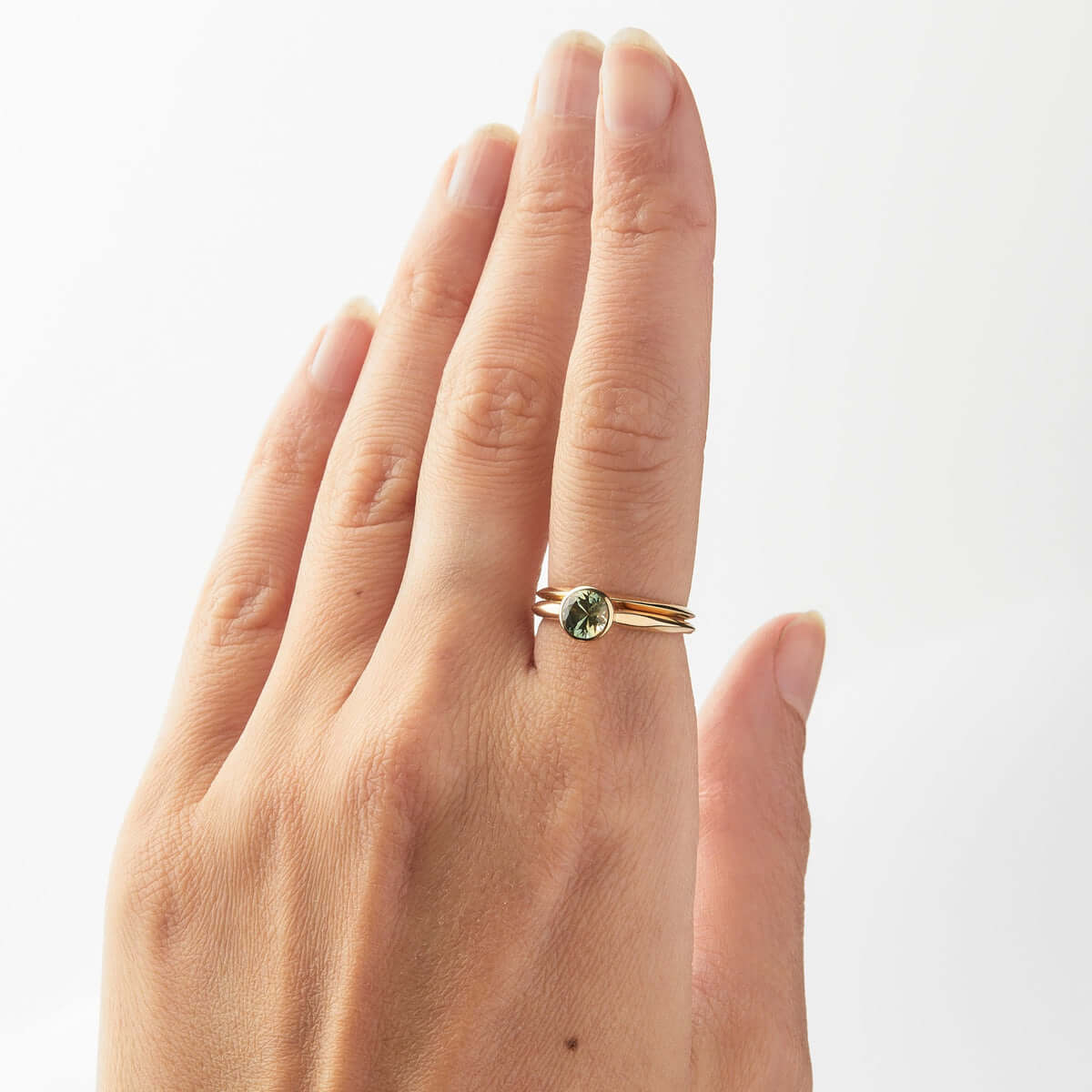 A hand showcasing a gold ring set with a round-cut Australian sapphire, alongside a simple gold band.