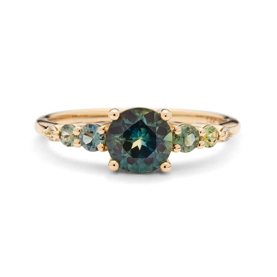 A yellow gold ring with an Australian sapphire encircled by two diamonds and green sapphires on a square band, set against a white background.