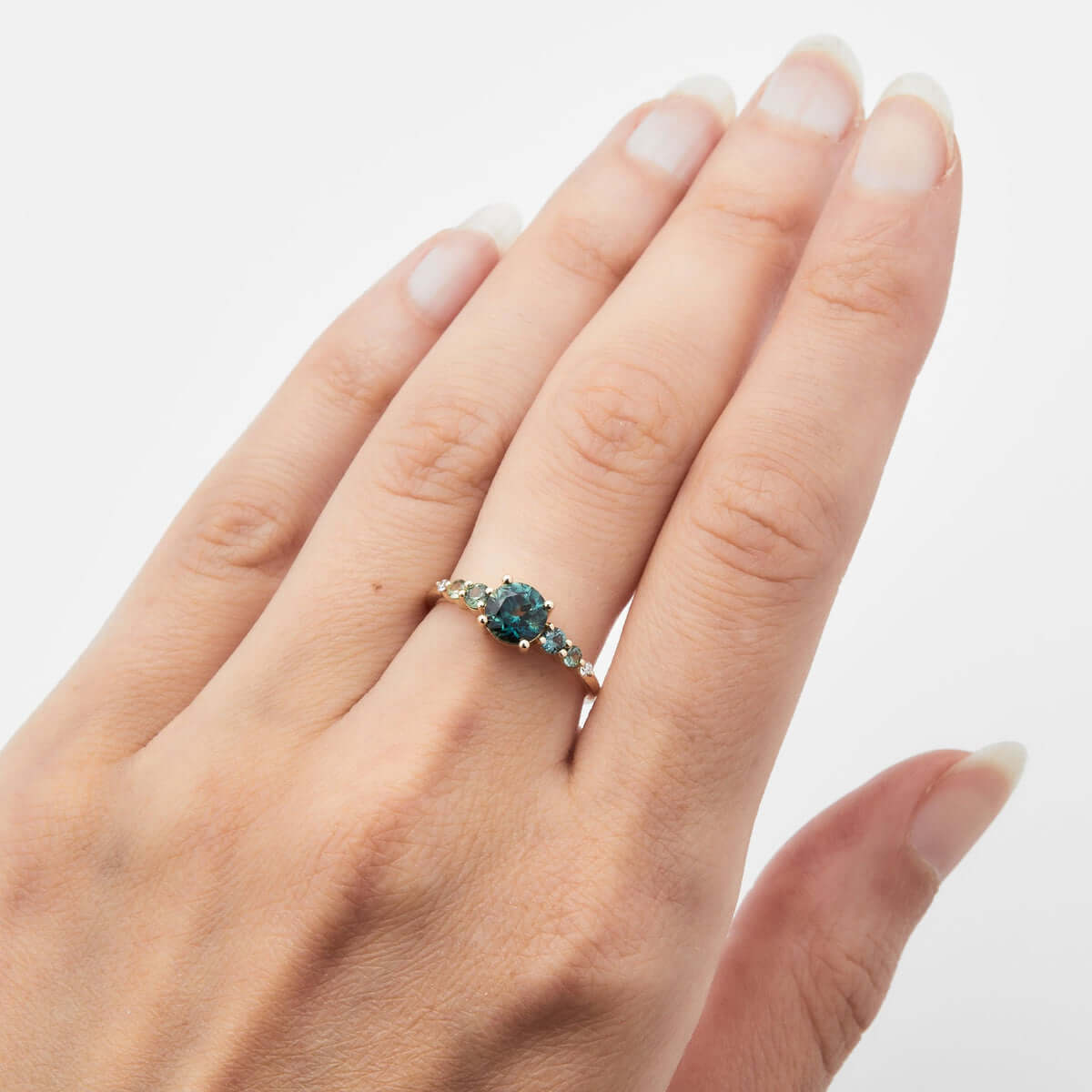 Overhead view of a hand wearing a yellow gold ring with an Australian sapphire, diamond details, and a square gold band.