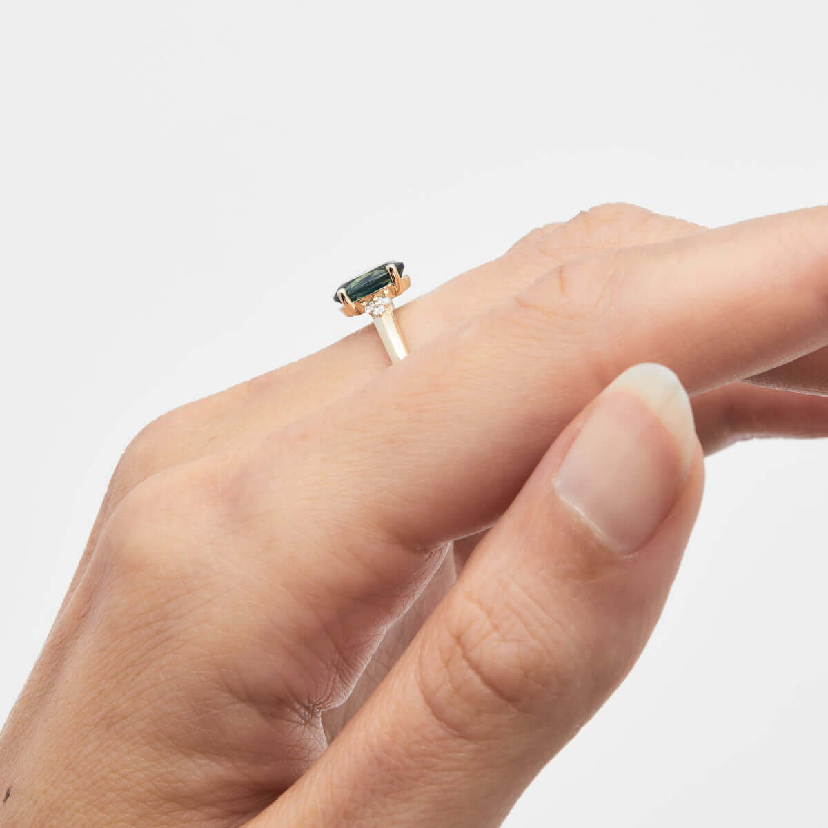 A side-view of a hand showcasing a yellow gold ring with a central teal Australian sapphire.