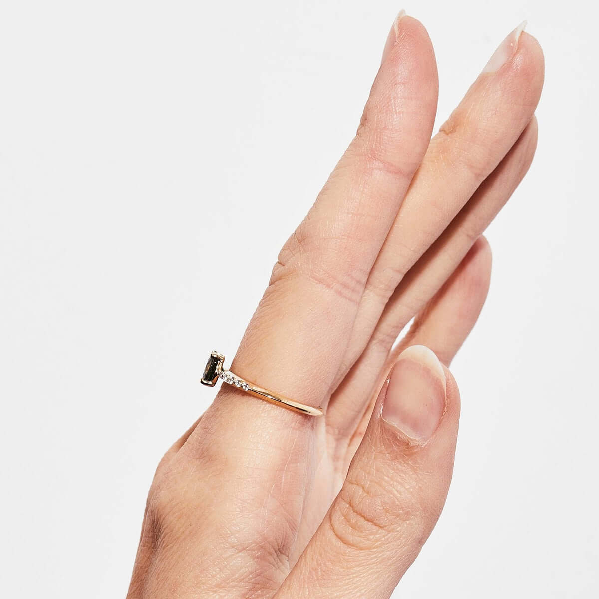 A hand model showing a side view of a yellow gold ring with a large sapphire gem and small diamonds.