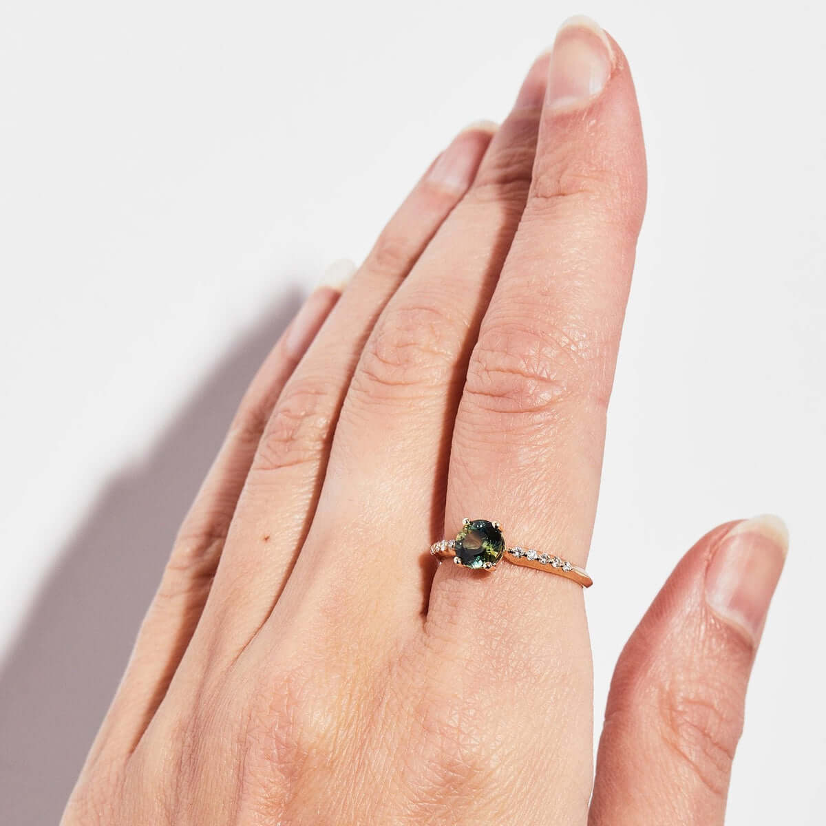 A hand wearing a yellow gold ring with a central bi-color Australian sapphire and a linear sequence of diamonds.
