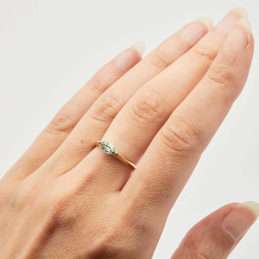 A yellow gold ring with a marquise Montana sapphire displayed on a finger.