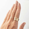 A hand wearing a stack of three gold signet rings, one featuring a small Australian sapphire and the other two a diamond.