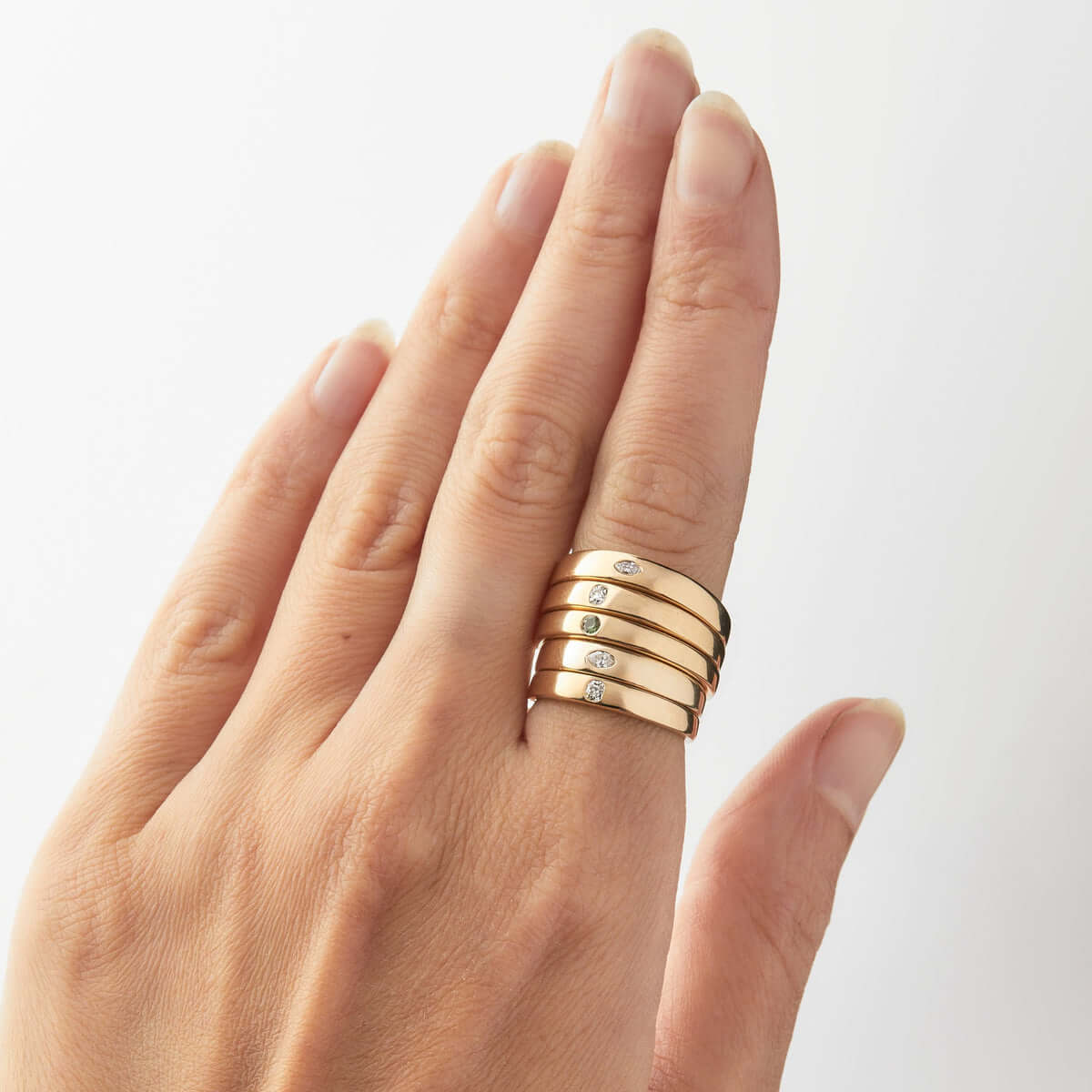 A hand wearing a stack of five gold signet rings, each featuring a small Australian sapphire or diamond. 