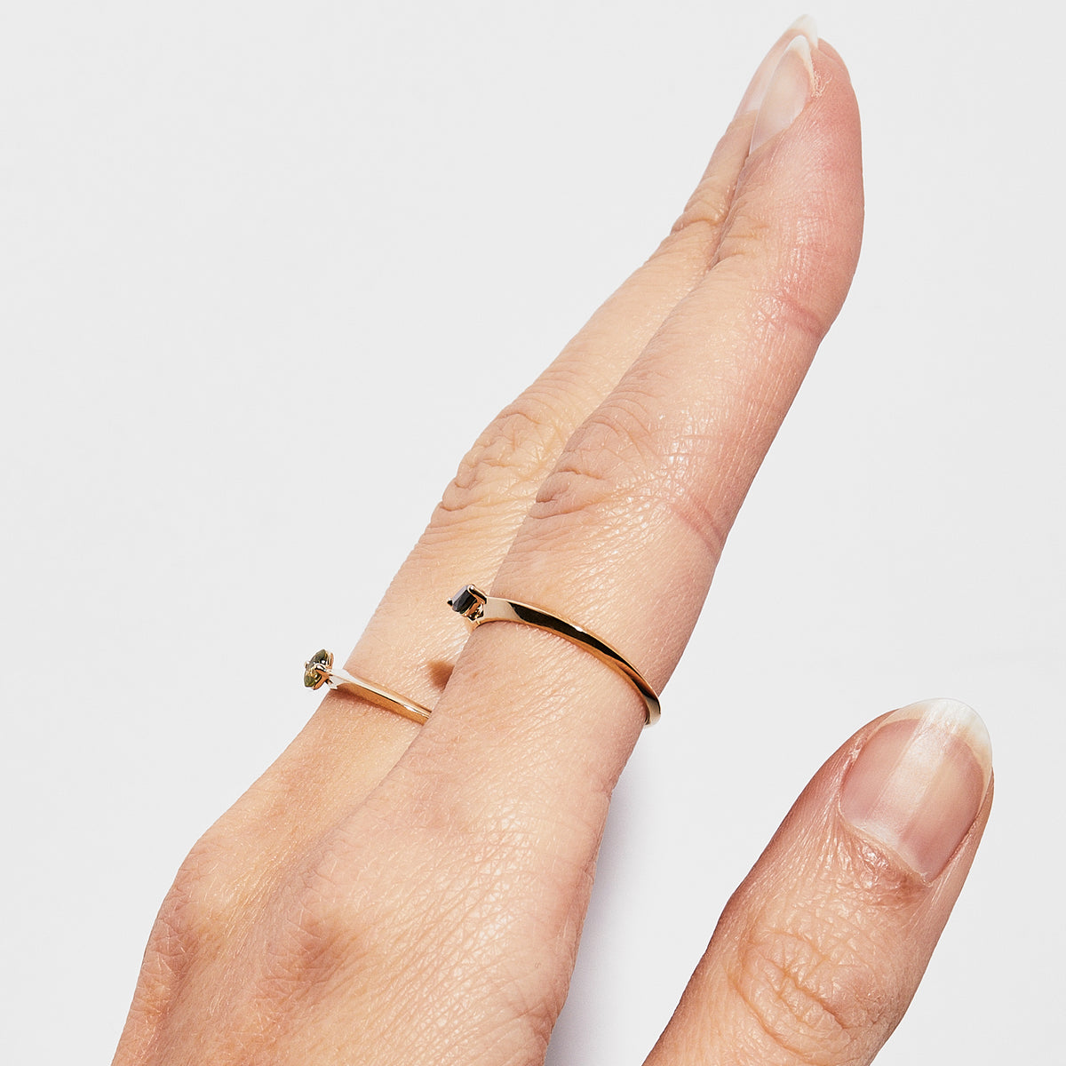 A person's hand showing a dainty 14K yellow gold ring worn on the ring finger. The ring features a small, green Australian Sapphire set at the center.