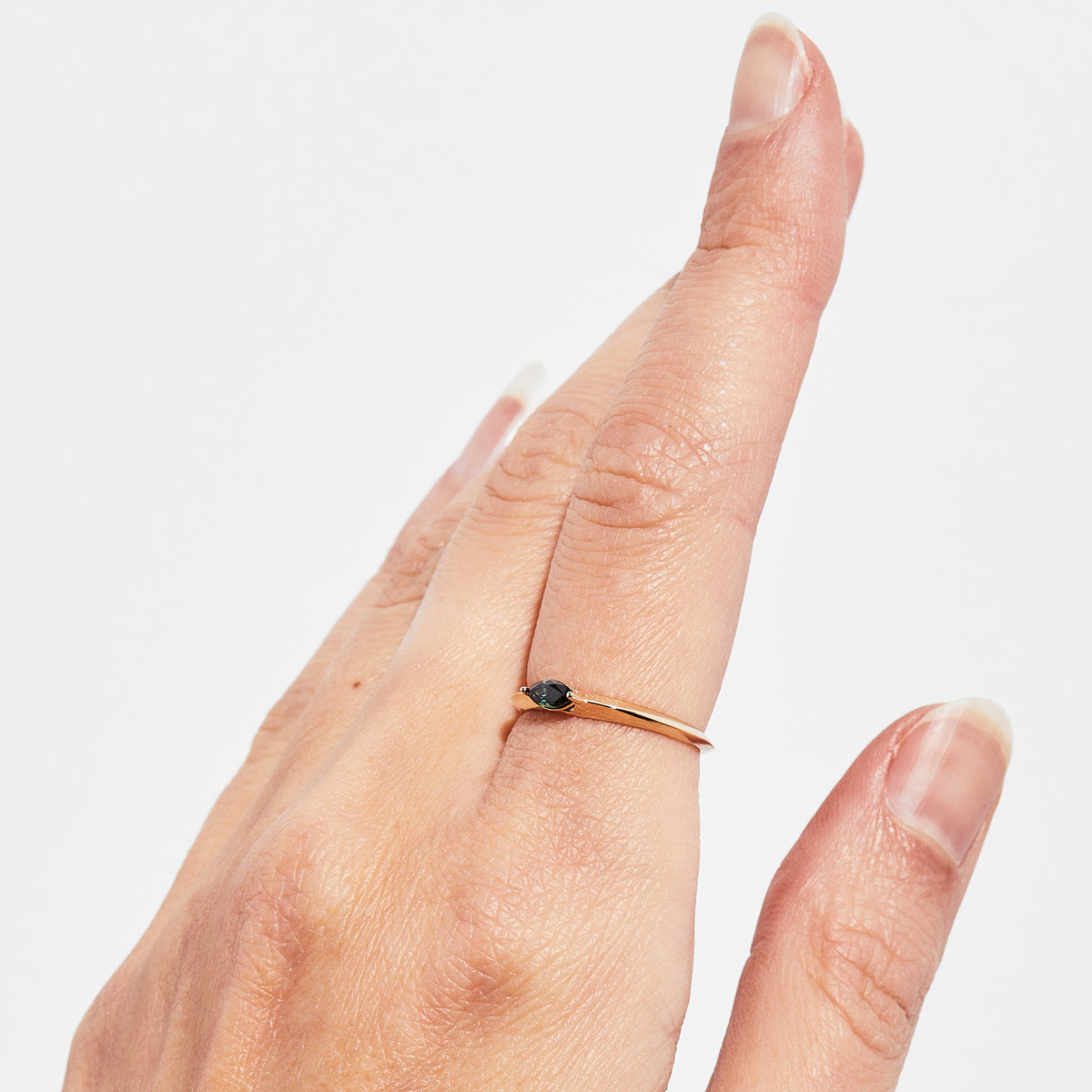 A hand wearing a ring, displaying how the thin 14K yellow gold band and a green Australian Sapphire.
