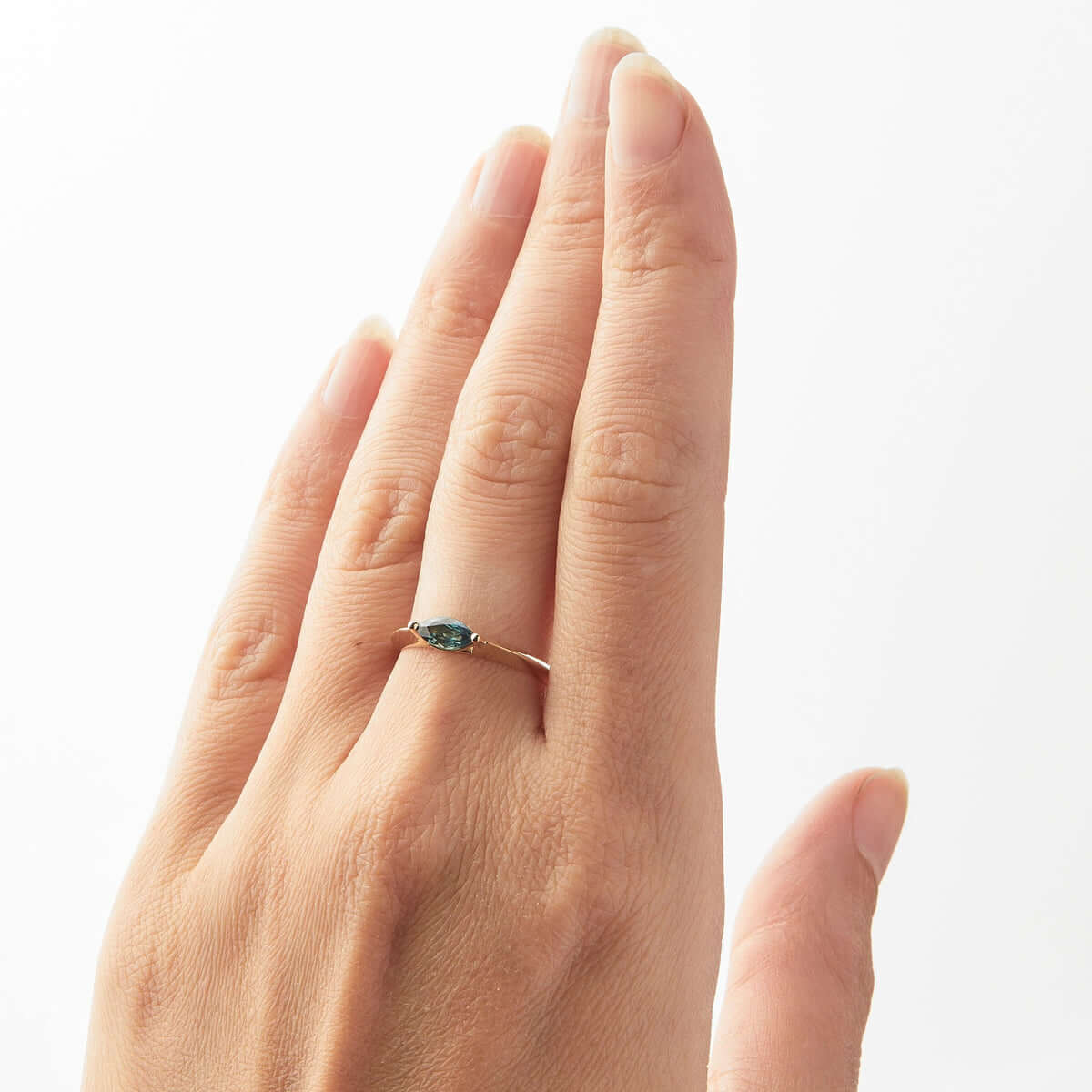 A hand model displaying a yellow gold ring with a marquise-cut Australian sapphire.
