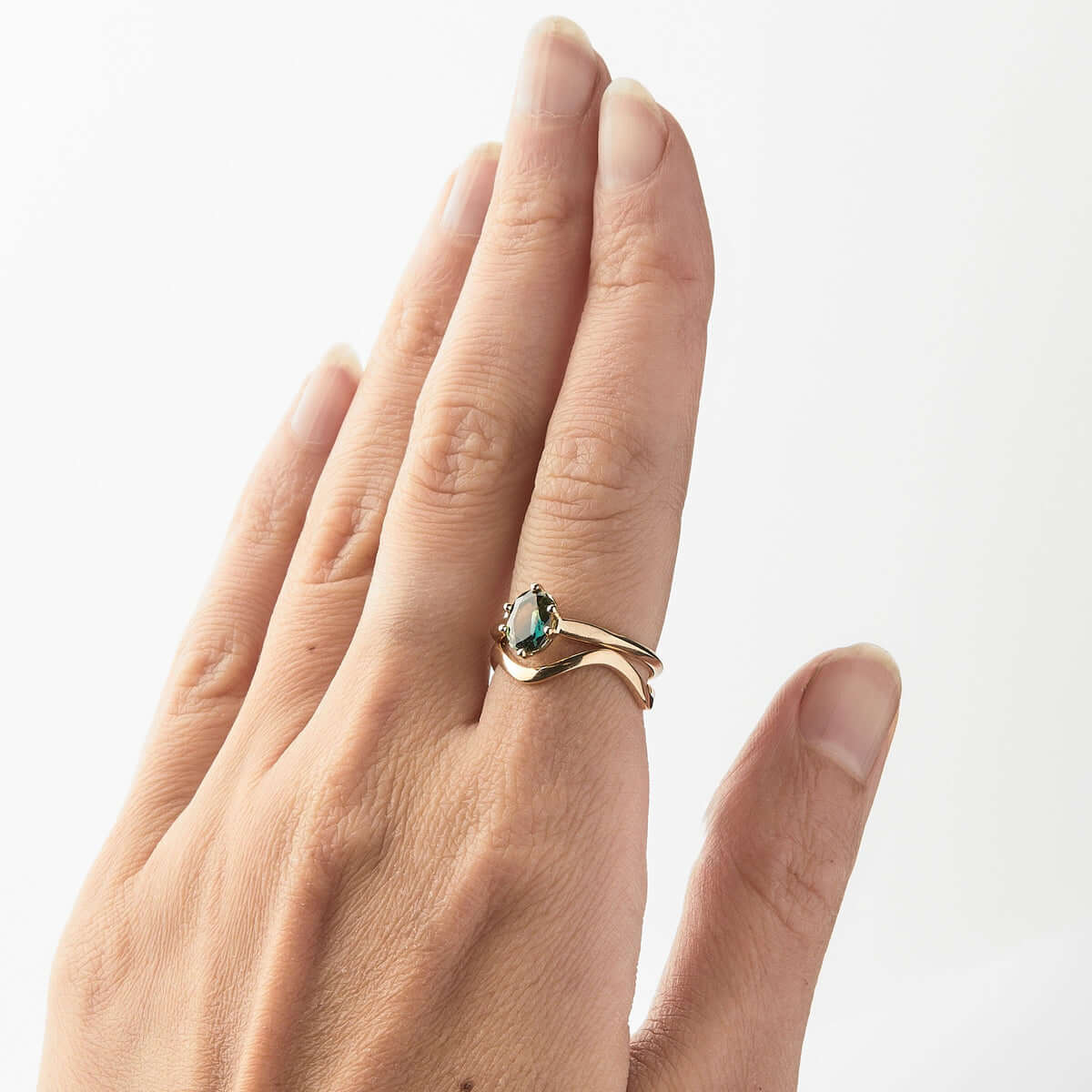 A hand showing off a yellow gold ring with an green oval Australian sapphire paired with a wavy gold band.