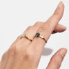 A hand wearing two rings on separate fingers. One a yellow gold ring with a round green Australian sapphire and the other a gold band with a white diamond.