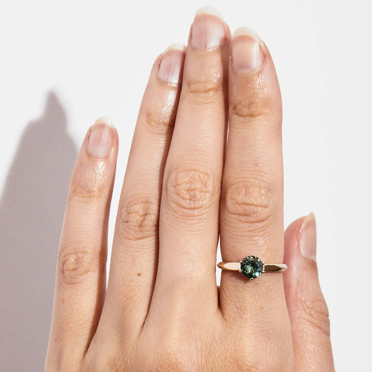 A hand with a beautiful yellow gold ring with a round green Australian sapphire.