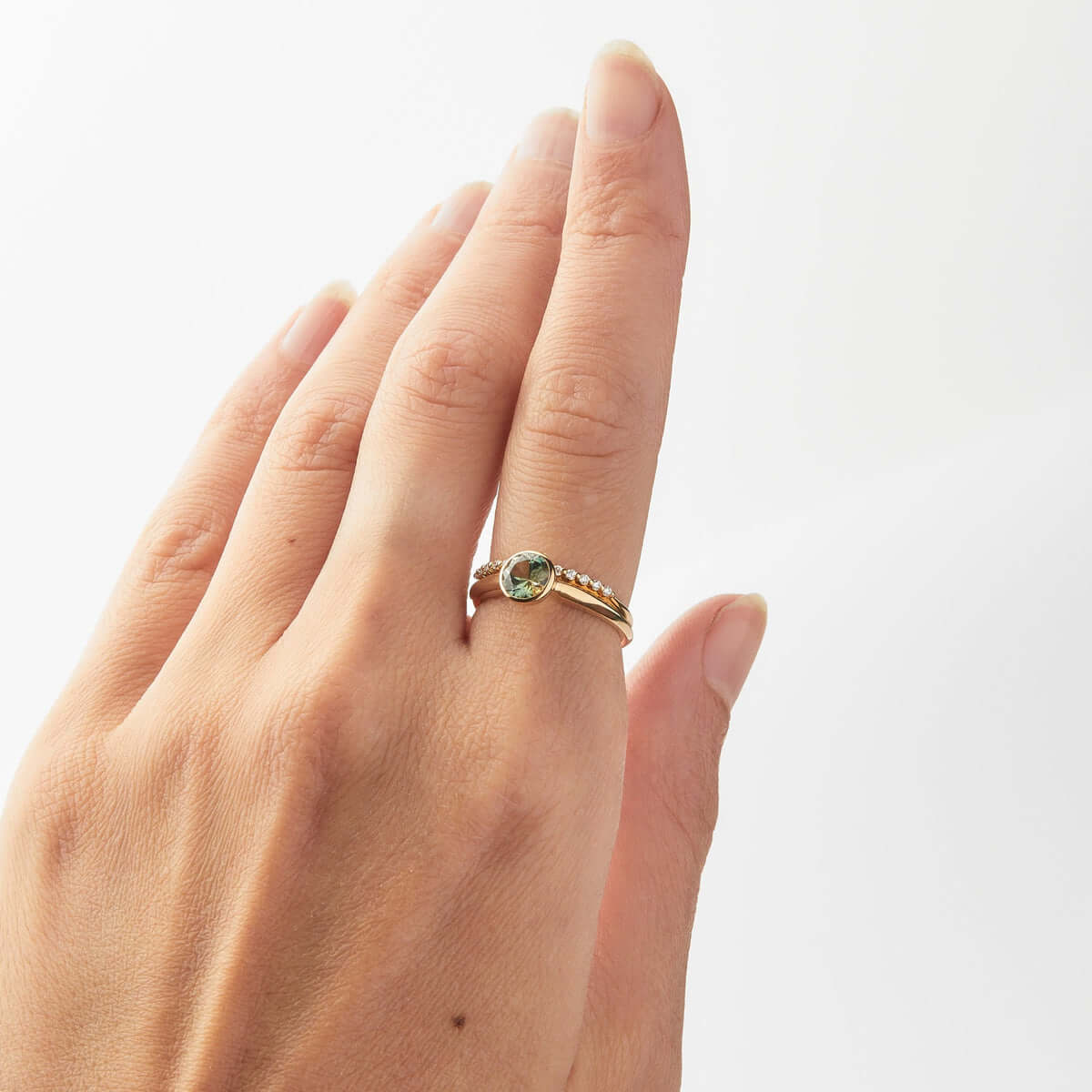 A hand model displaying a gold ring with a bezel-set, round-cut Australian sapphire, paired with a diamond gold band.