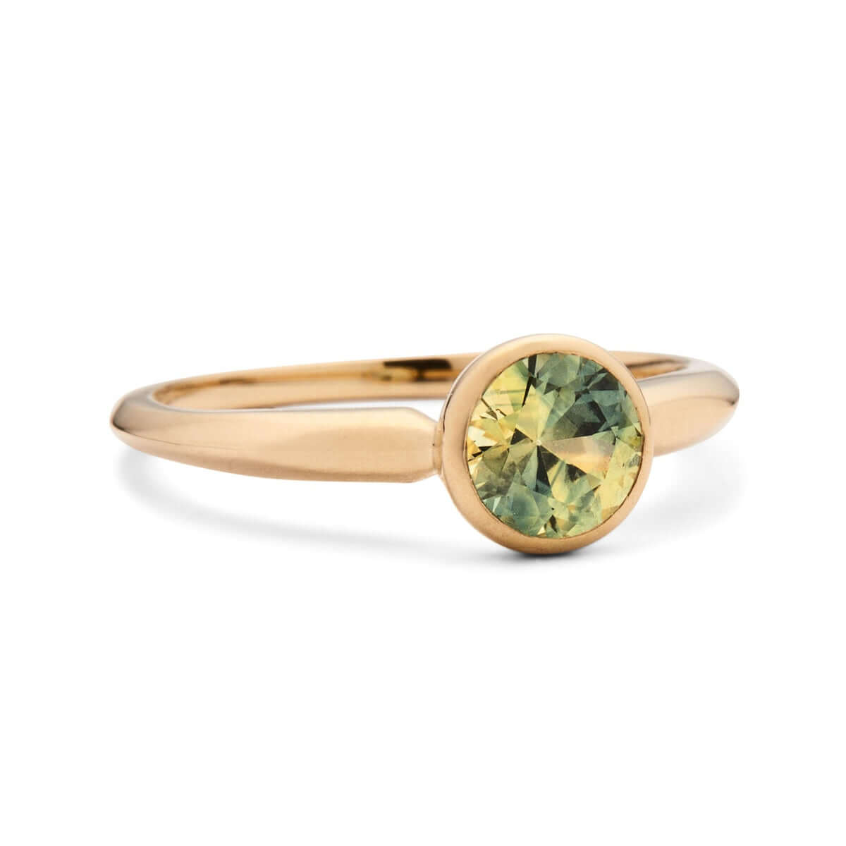 A side-angled view of a simple yet elegant gold ring with a bezel setting, showcasing a round-cut Australian sapphire with a soft greenish hue, on a white backdrop.