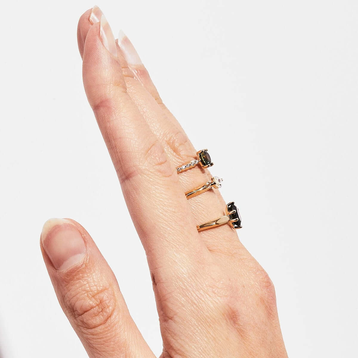 A hand model showing a side view of 3x gold rings featuring sapphires and white diamonds. 